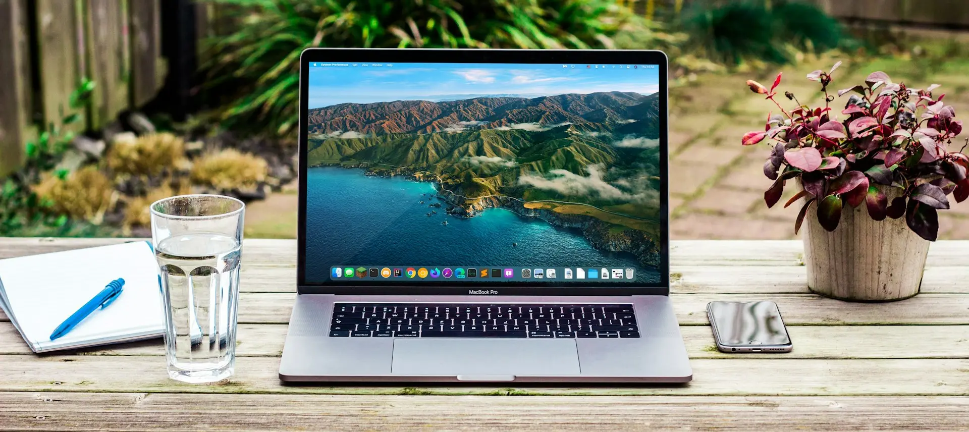 macbook pro beside clear drinking glass on brown wooden table